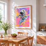 Astronaut in orange splatter cross stitch artwork displayed on wall as home decor