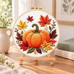 Autumn pumpkin and maple leaves embroidery kit finished hoop displayed on a wooden stand as cosy tabletop decor