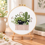 Black cat and cactus embroidery kit finished hoop displayed on a wooden stand as cosy tabletop decor