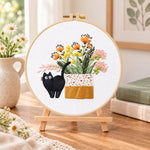 Black cat and wildflowers embroidery kit finished hoop displayed on a wooden stand as cosy tabletop decor