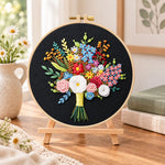Black fabric flower bouquet embroidery kit finished hoop displayed on a wooden stand as cosy tabletop decor