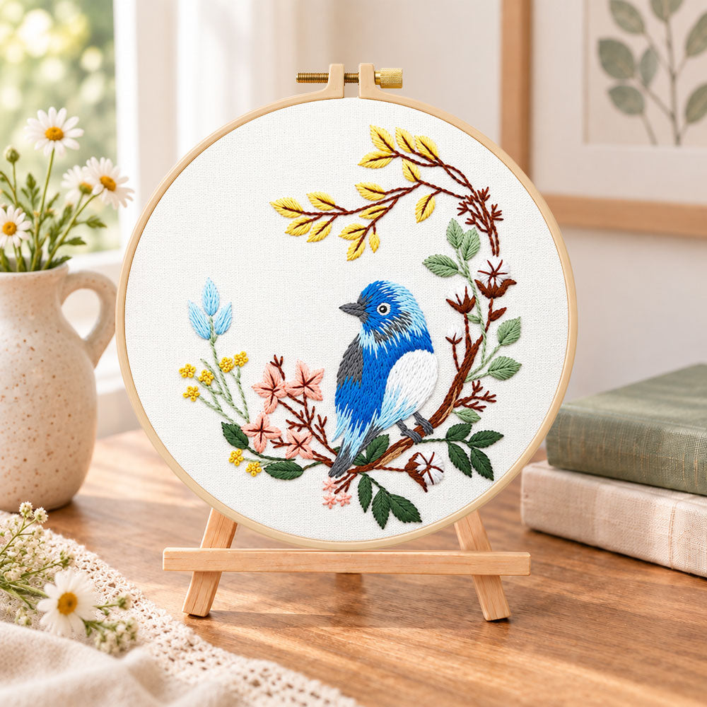 Blue bird on floral branch embroidery kit finished hoop displayed on a wooden stand as cosy tabletop decor