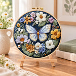 Blue butterfly in wildflower garden embroidery kit finished hoop displayed on a wooden stand as cozy tabletop decor
