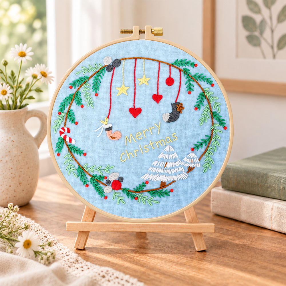 Blue christmas wreath embroidery kit finished hoop displayed on a wooden stand as cosy tabletop decor