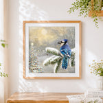 Finished blue jay in snow cross stitch artwork displayed
