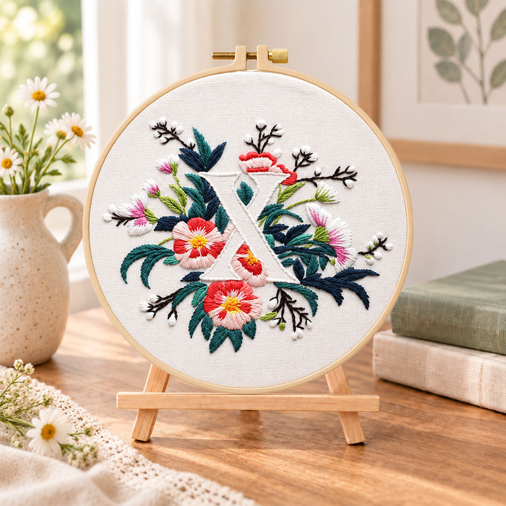 Blush florals and letter x embroidery kit finished hoop displayed on a wooden stand as cosy tabletop decor