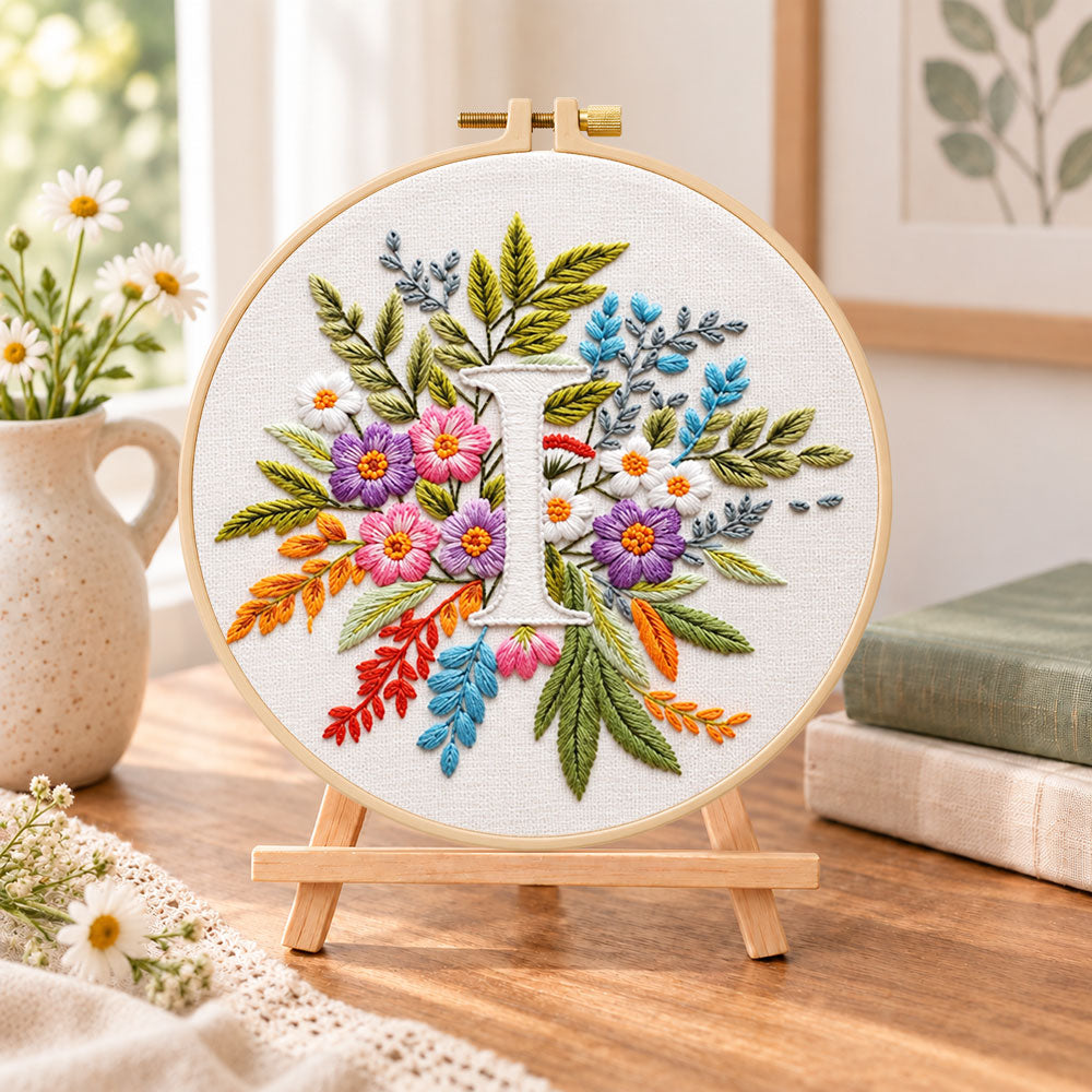 Bright mixed petals and letter i embroidery kit finished hoop displayed on a wooden stand as cosy tabletop decor