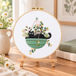 Cat in green hanging pot embroidery kit finished hoop displayed on a wooden stand as cosy tabletop decor