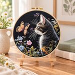 Cat watching butterfly embroidery kit finished hoop displayed on a wooden stand as cosy tabletop decor
