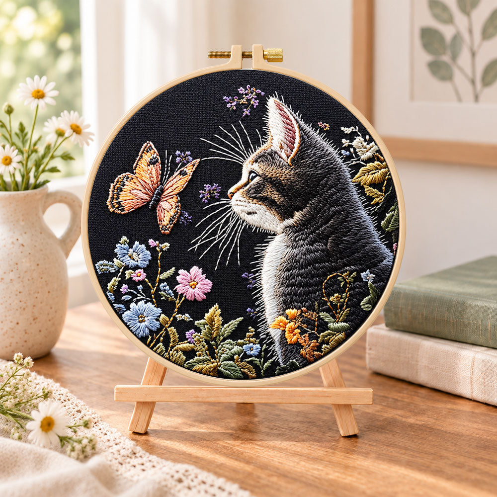 Cat watching butterfly embroidery kit finished hoop displayed on a wooden stand as cosy tabletop decor