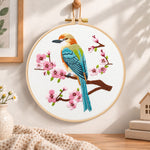 Colourful bird amid pink cherry blossoms embroidery hoop wall art displayed as warm and cosy handmade home decor