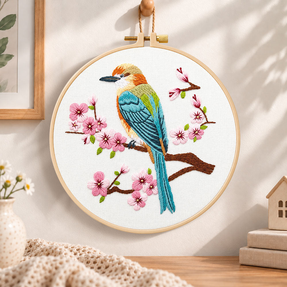 Colourful bird amid pink cherry blossoms embroidery hoop wall art displayed as warm and cosy handmade home decor