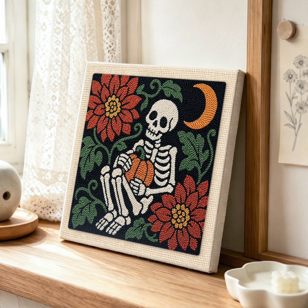 Cosy skeleton holding pumpkin punch needle artwork displayed on a table
