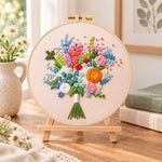 Cream wildflower bouquet embroidery kit finished hoop displayed on a wooden stand as cosy tabletop decor