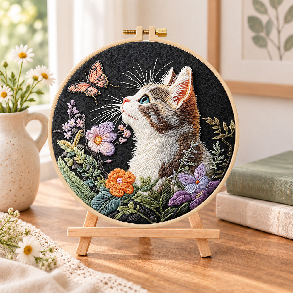 Curious cat and pink butterfly embroidery kit finished hoop displayed on a wooden stand as cosy tabletop decor