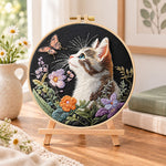 Curious cat and pink butterfly embroidery kit finished hoop displayed on a wooden stand as cosy tabletop decor