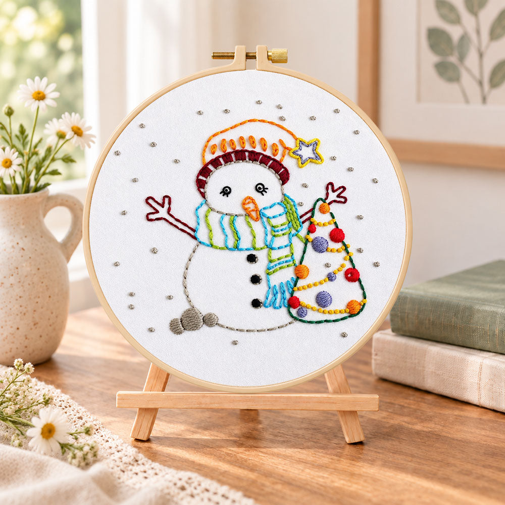 Cute snowman and tree embroidery kit finished hoop displayed on a wooden stand as cosy tabletop decor