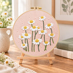 Daisies on dusty pink fabric embroidery kit finished hoop displayed on a wooden stand as cosy tabletop decor