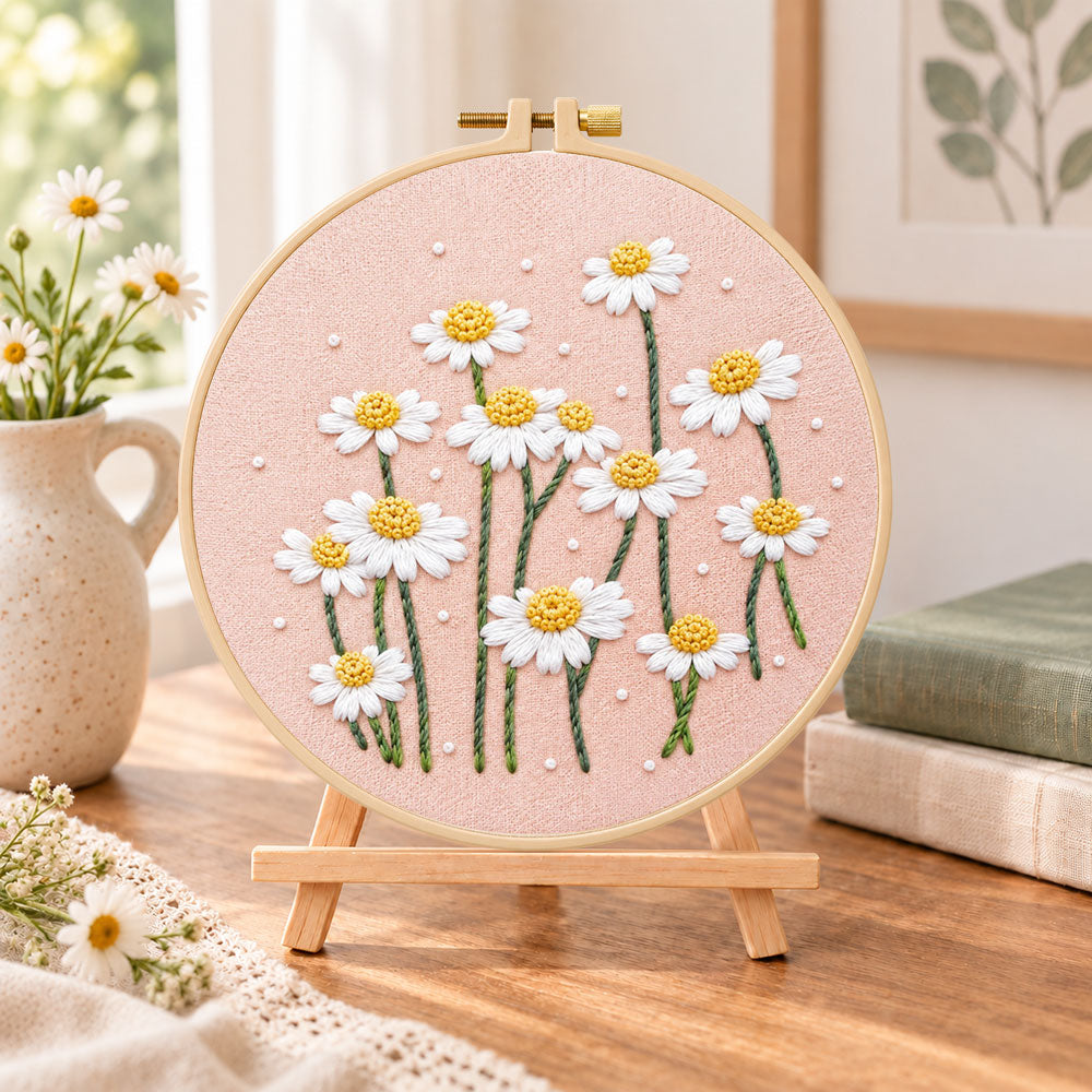 Daisies on dusty pink fabric embroidery kit finished hoop displayed on a wooden stand as cosy tabletop decor