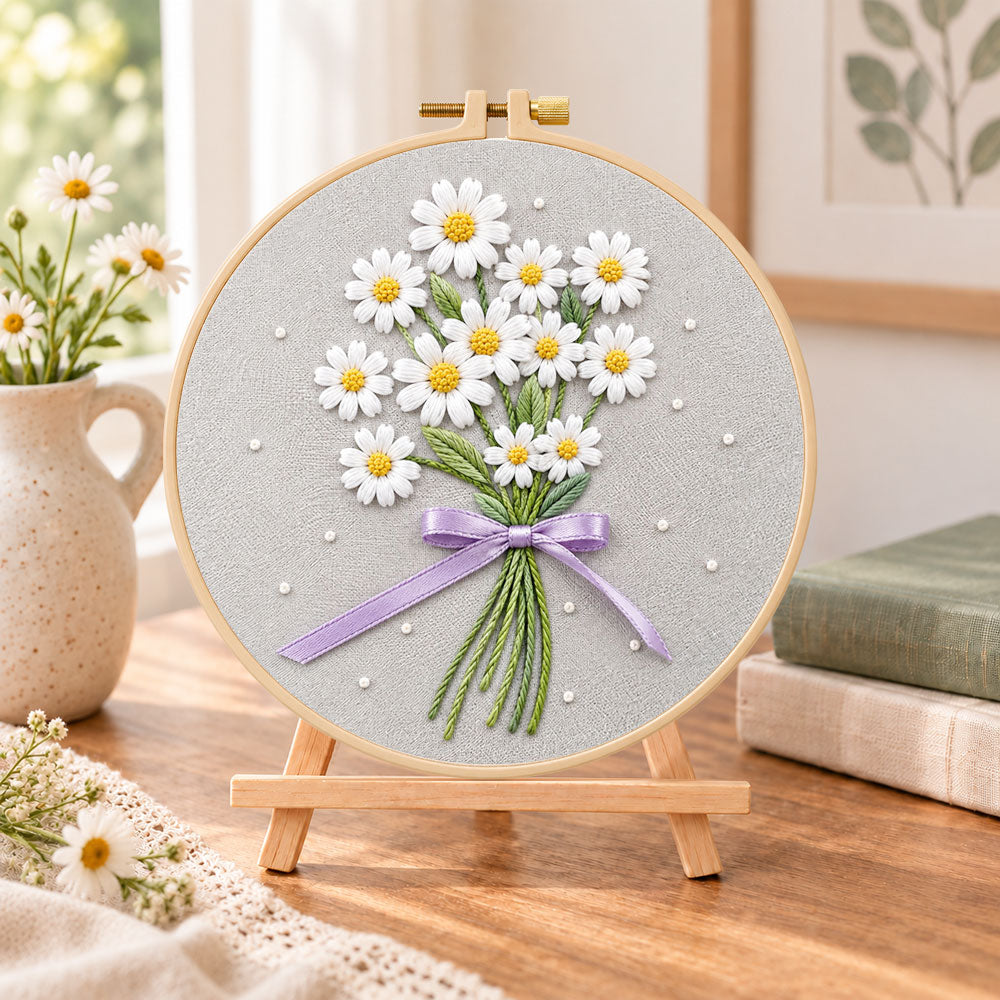 Daisy bouquet with purple ribbon embroidery kit finished hoop displayed on a wooden stand as cosy tabletop decor