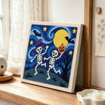 Dancing skeletons under moon punch needle artwork displayed on a table