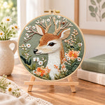 Deer and wild daisies embroidery kit finished hoop displayed on a wooden stand as cosy tabletop decor