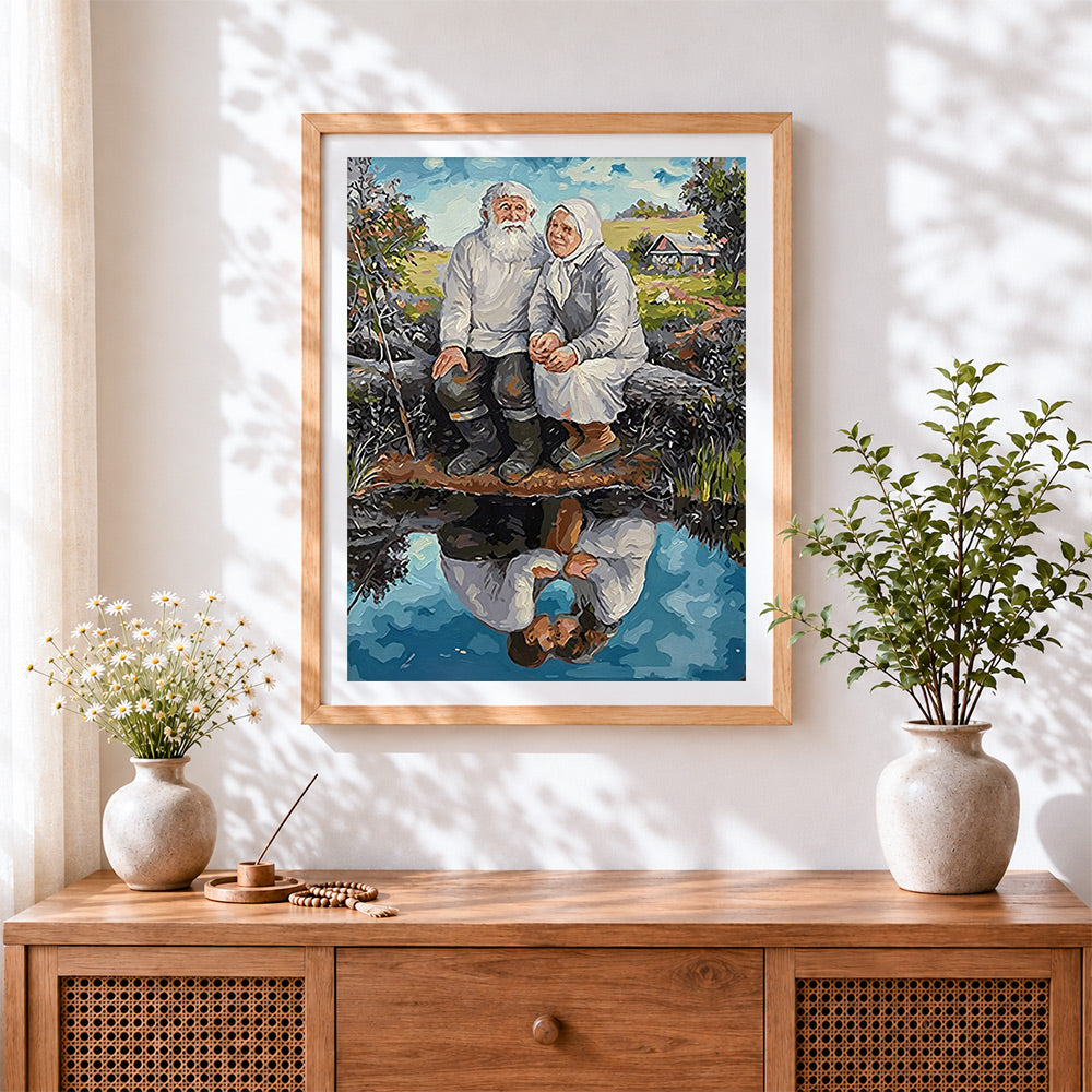 Finished elderly couple sitting by water cross stitch artwork displayed