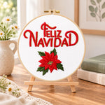 Feliz navidad poinsettia embroidery kit finished hoop displayed on a wooden stand as cozy tabletop decor