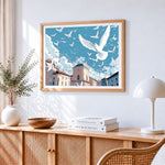 Flock of white doves flying over a city cross stitch artwork displayed on wall as home decor