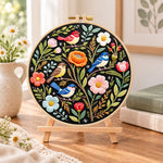 Forest birds and spring blooms embroidery kit finished hoop displayed on a wooden stand as cosy tabletop decor