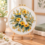 Golden florals and letter a embroidery kit finished hoop displayed on a wooden stand as cosy tabletop decor