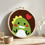 Green dinosaur and red heart punch needle artwork displayed on a table