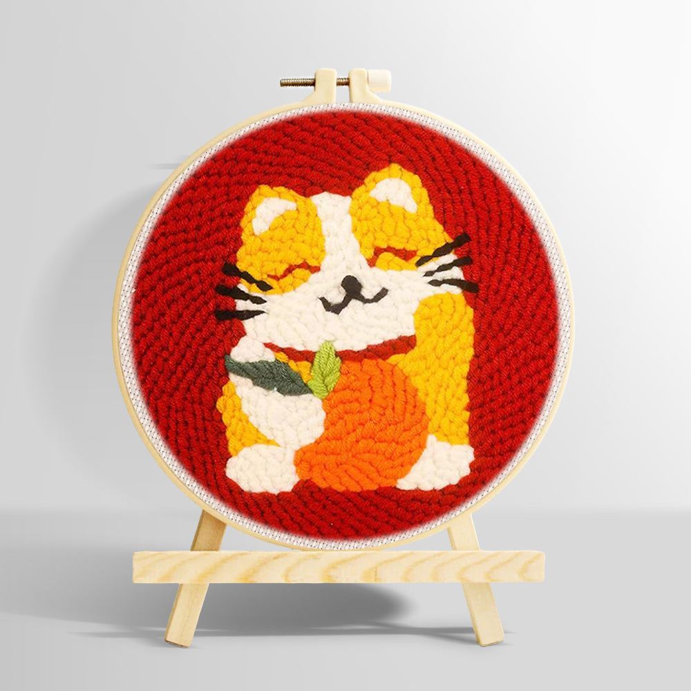 Happy cat holding an orange punch needle kit for beginners