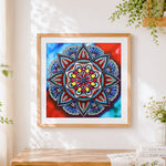Finished jewel tone red and blue mandala cross stitch artwork displayed