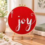 Joy christmas script embroidery kit finished hoop displayed on a wooden stand as cozy tabletop decor