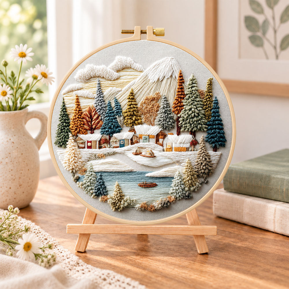 Lakeside snow town embroidery kit finished hoop displayed on a wooden stand as cosy tabletop decor