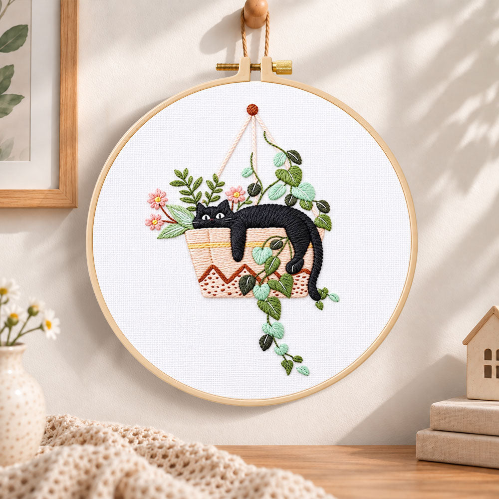 Lazy cat in hanging planter embroidery hoop wall art displayed as warm and cosy handmade home decor