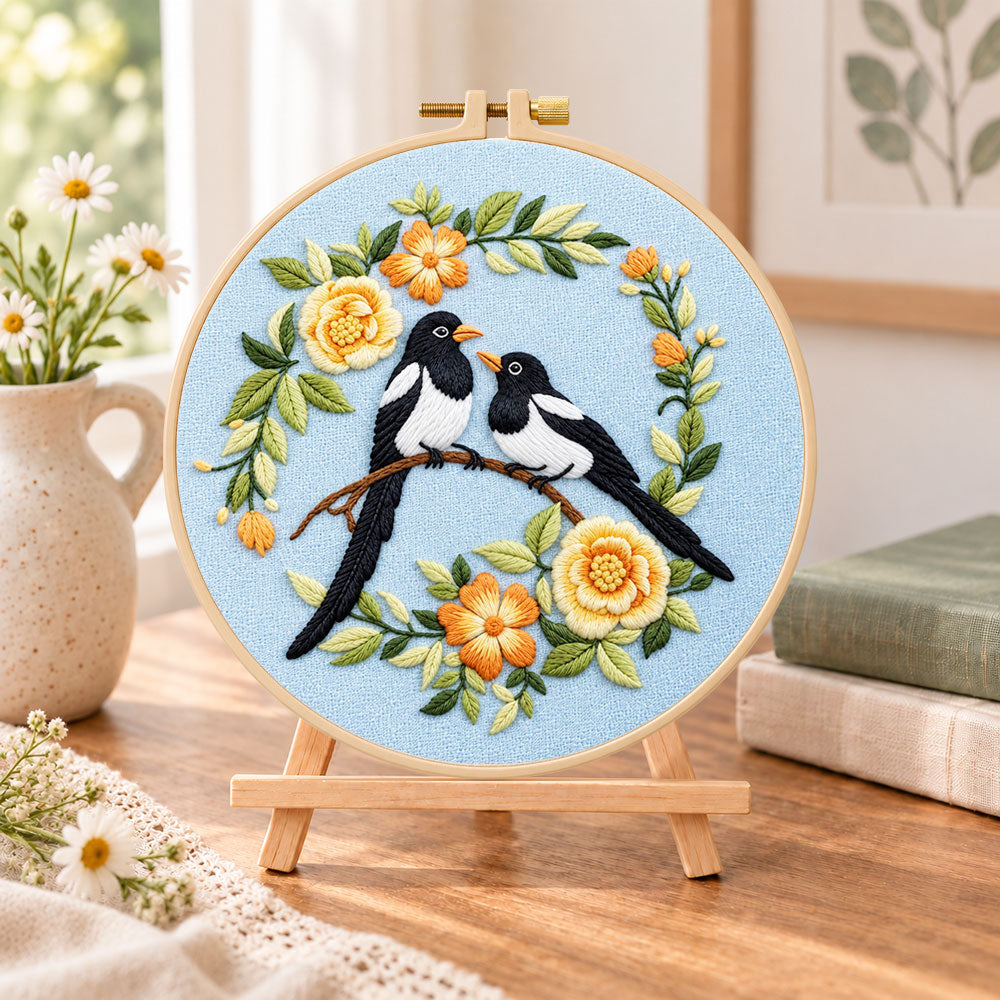 Magpie pair with yellow flowers embroidery kit finished hoop displayed on a wooden stand as cosy tabletop decor