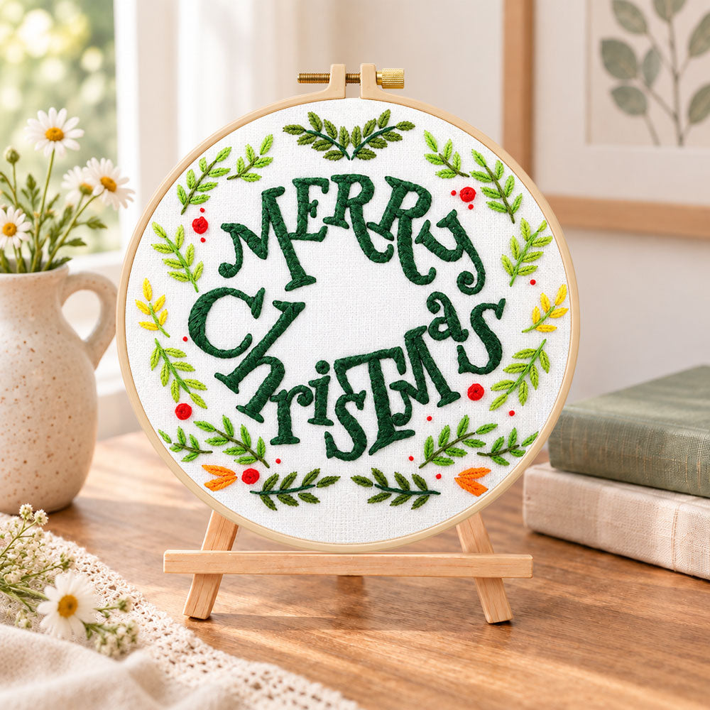 Merry christmas wreath embroidery kit finished hoop displayed on a wooden stand as cosy tabletop decor