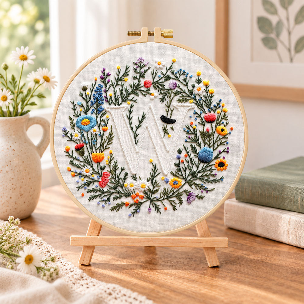 Mixed floral wreath and letter w embroidery kit finished hoop displayed on a wooden stand as cosy tabletop decor