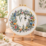 Mixed floral wreath and letter w embroidery kit finished hoop displayed on a wooden stand as cosy tabletop decor