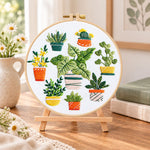 Mixed mini potted greenery embroidery kit finished hoop displayed on a wooden stand as cosy tabletop decor