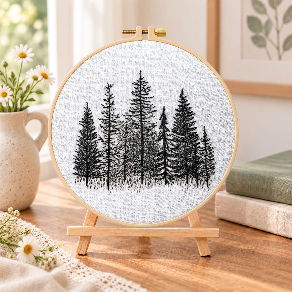 Monochrome pine woods embroidery kit finished hoop displayed on a wooden stand as cosy tabletop decor
