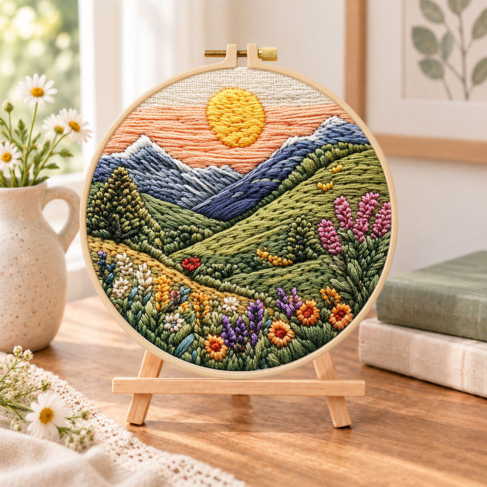 Mountain sunset meadow embroidery kit finished hoop displayed on a wooden stand as cozy tabletop decor