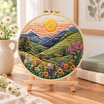 Mountain sunset meadow embroidery kit finished hoop displayed on a wooden stand as cozy tabletop decor
