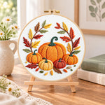 Multiple pumpkins with autumn leaves embroidery kit finished hoop displayed on a wooden stand as cosy tabletop decor
