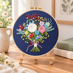 Navy floral bouquet embroidery kit finished hoop displayed on a wooden stand as cosy tabletop decor
