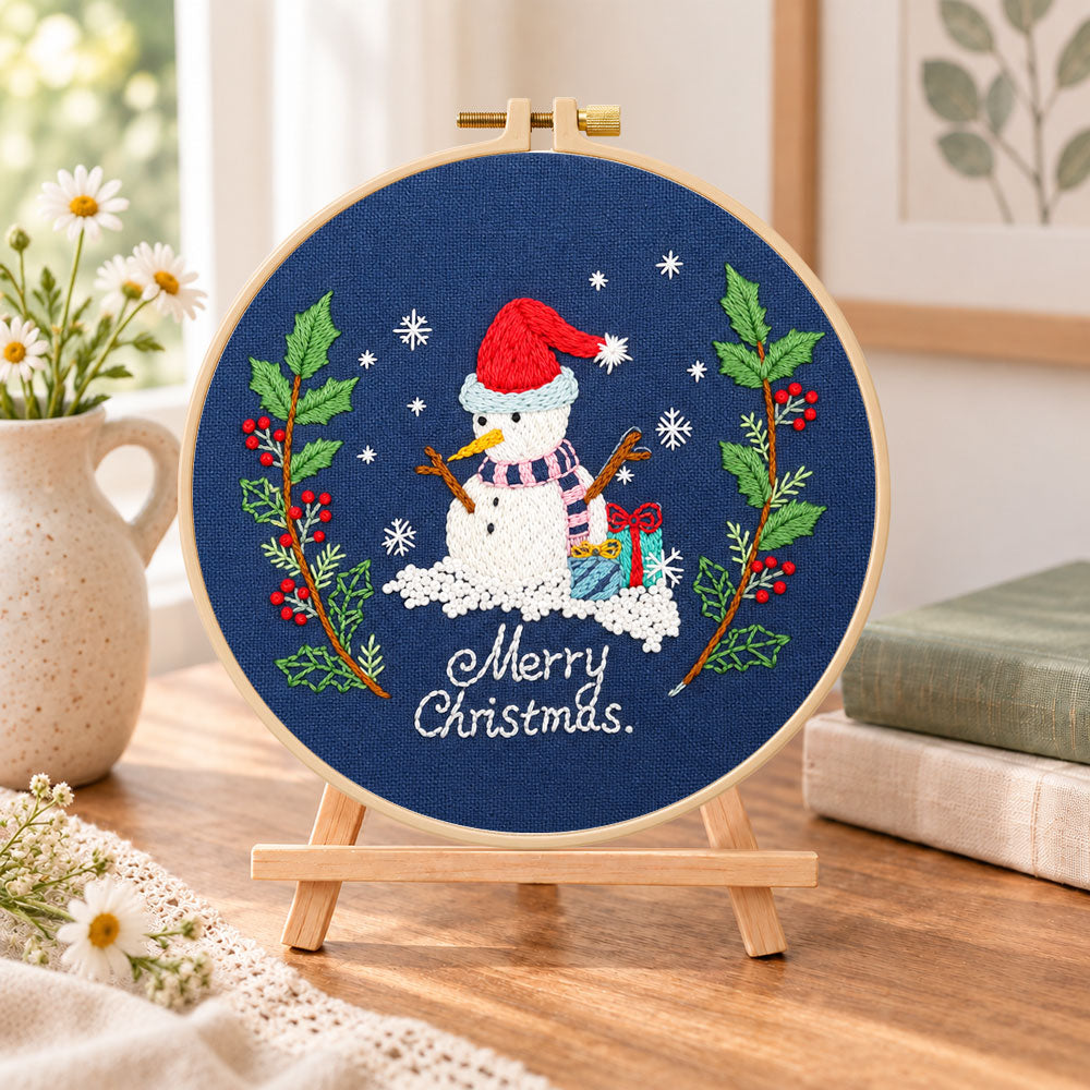 Navy snowman art embroidery kit finished hoop displayed on a wooden stand as cosy tabletop decor