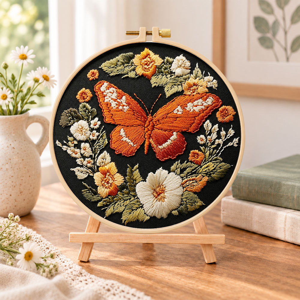 Orange butterfly amid blooms embroidery kit finished hoop displayed on a wooden stand as cozy tabletop decor