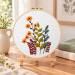 Orange daisy floral sprig embroidery kit finished hoop displayed on a wooden stand as cosy tabletop decor